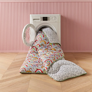 Washing machine with colourful rainbow duvet and a pink wall in the background