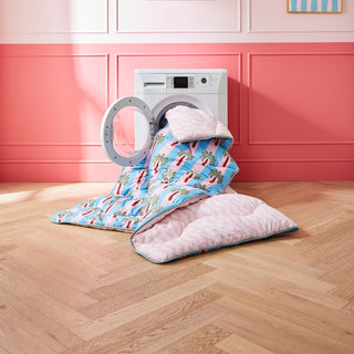 White washing machine with a colorful towel duvet over it in a room with pink walls and framed pictures.